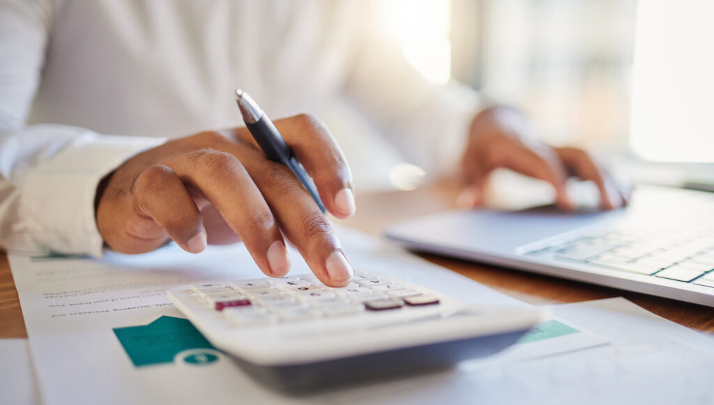 Person using a laptop and calculator to calculate costs